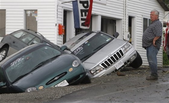 Rene Crete looks over damaged cars at Buy Right Auto on Friday in East Montpelier, Vt. Schools and roads are closed across central Vermont as heavy overnight rains caused flooding that overflowed riverbanks.